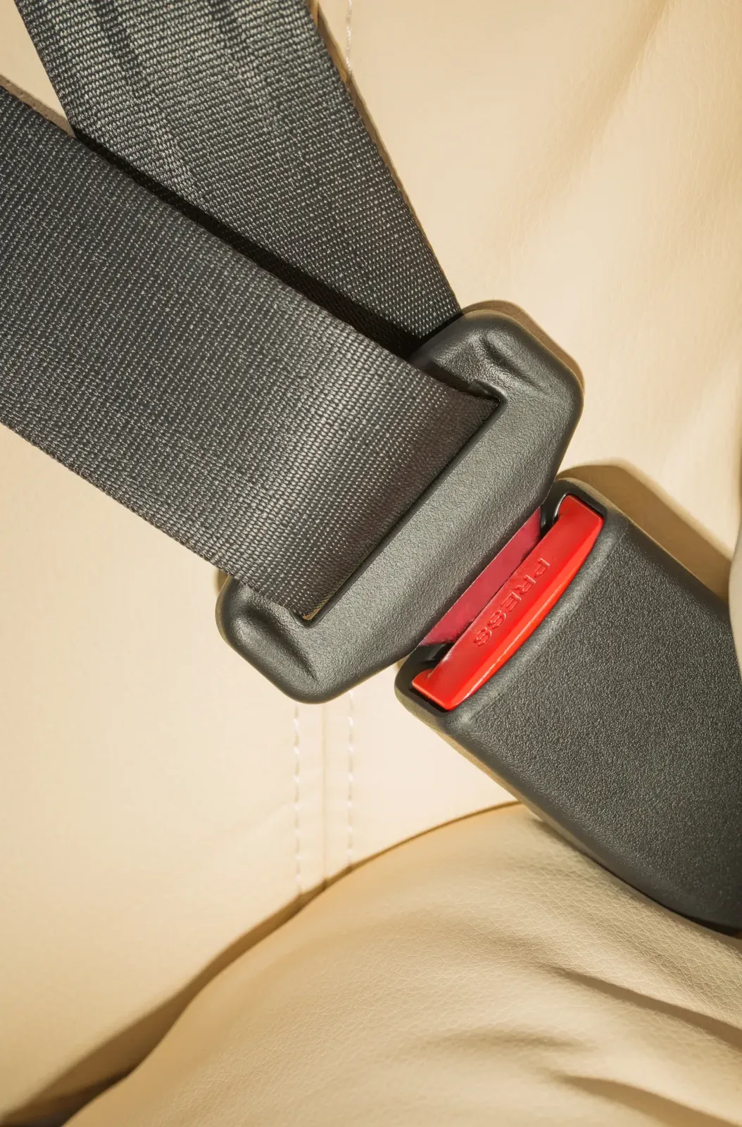 Seat belt webbing running down across a light-coloured vehicle seat into the buckle.